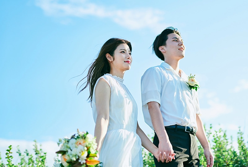 ブーケを手に持ち、自然の中を手をつないで歩く新婦と新郎の写真